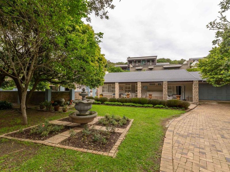 Front view of the property featuring a paved driveway, a well-maintained garden with a stone fountain, and a covered patio area.