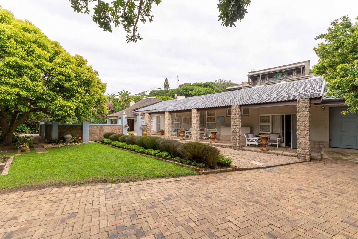 Rear view of the property featuring a covered patio with stone pillars, a paved driveway, and a well-maintained garden area.
