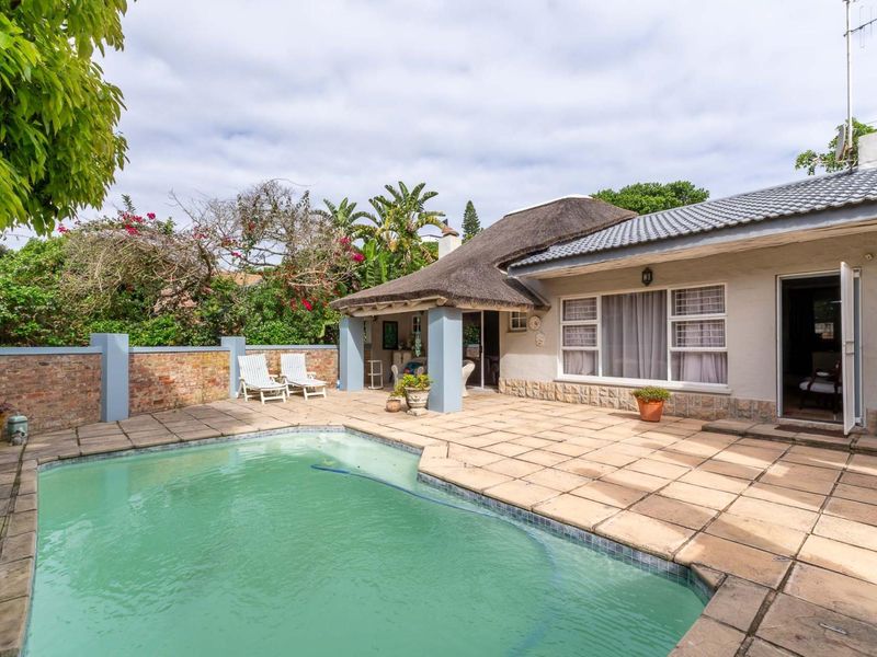 Outdoor pool area featuring a paved patio, thatched roof section, and brick boundary wall, providing a functional space for outdoor relaxation.