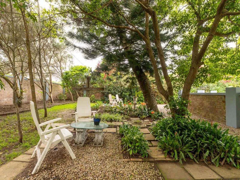 A private garden area featuring mature trees, established garden beds, stone paving, and a brick boundary wall.