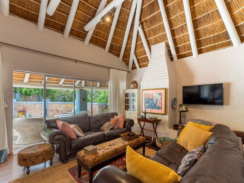 Spacious living room featuring a high vaulted thatched ceiling with exposed rafters, a traditional brick fireplace, and sliding doors leading to the patio.