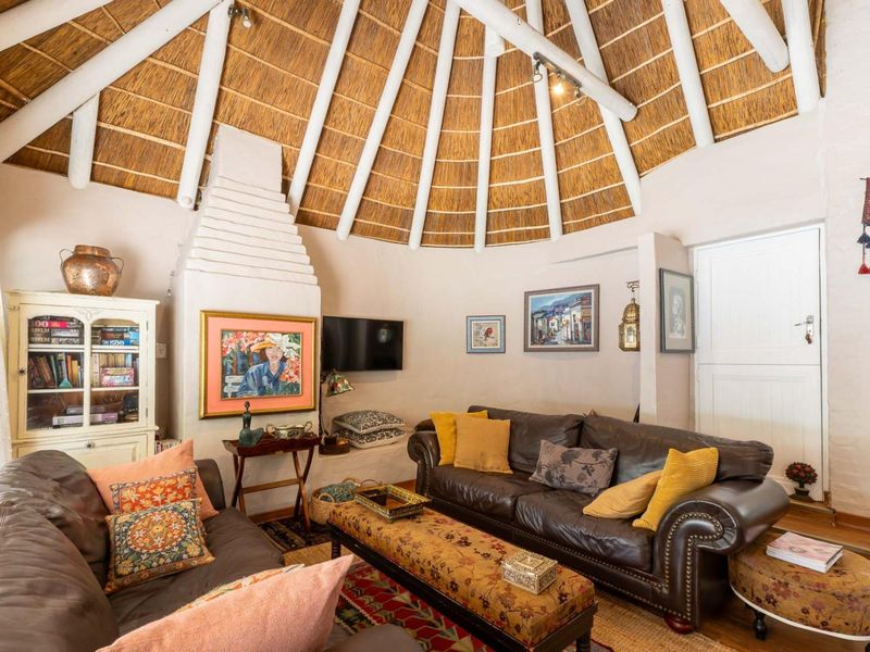 A cozy living room featuring a unique circular layout with a high thatched roof, exposed timber rafters, and a traditional built-in masonry fireplace.