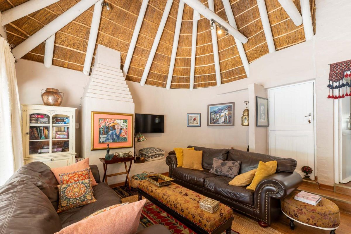 A cozy living room featuring a unique circular layout with a high thatched roof, exposed timber rafters, and a traditional built-in masonry fireplace.