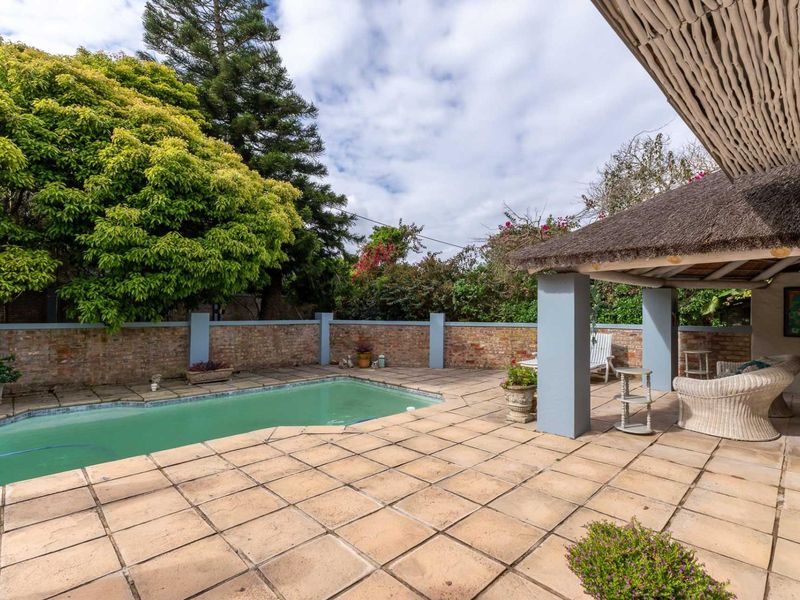 Outdoor pool area featuring a paved patio, a covered thatched roof entertainment space, and a brick boundary wall.