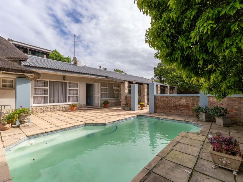 Outdoor pool area featuring a paved patio, brick boundary walls, and a mix of thatched and tiled roofing on the main house structure.