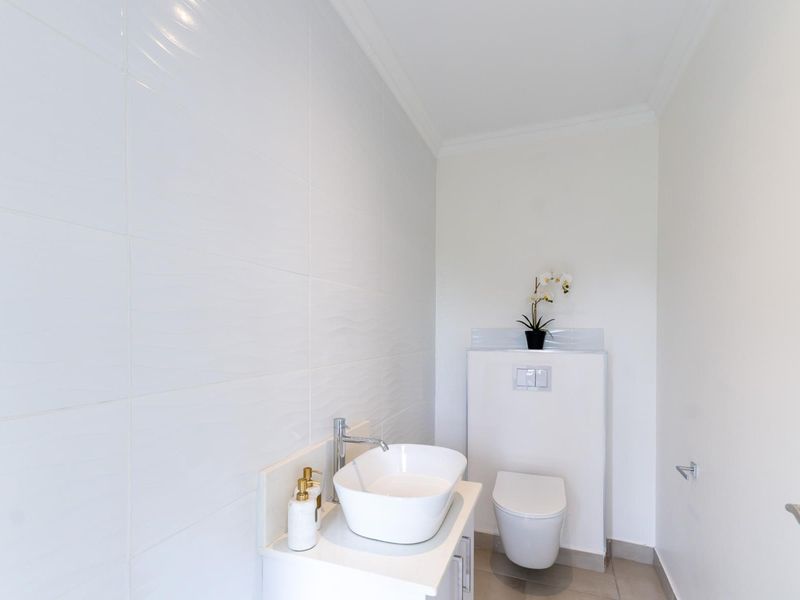 A modern, minimalist bathroom featuring a wall-mounted toilet with a concealed cistern, a sleek vessel sink on a vanity cabinet, and clean white tiling.