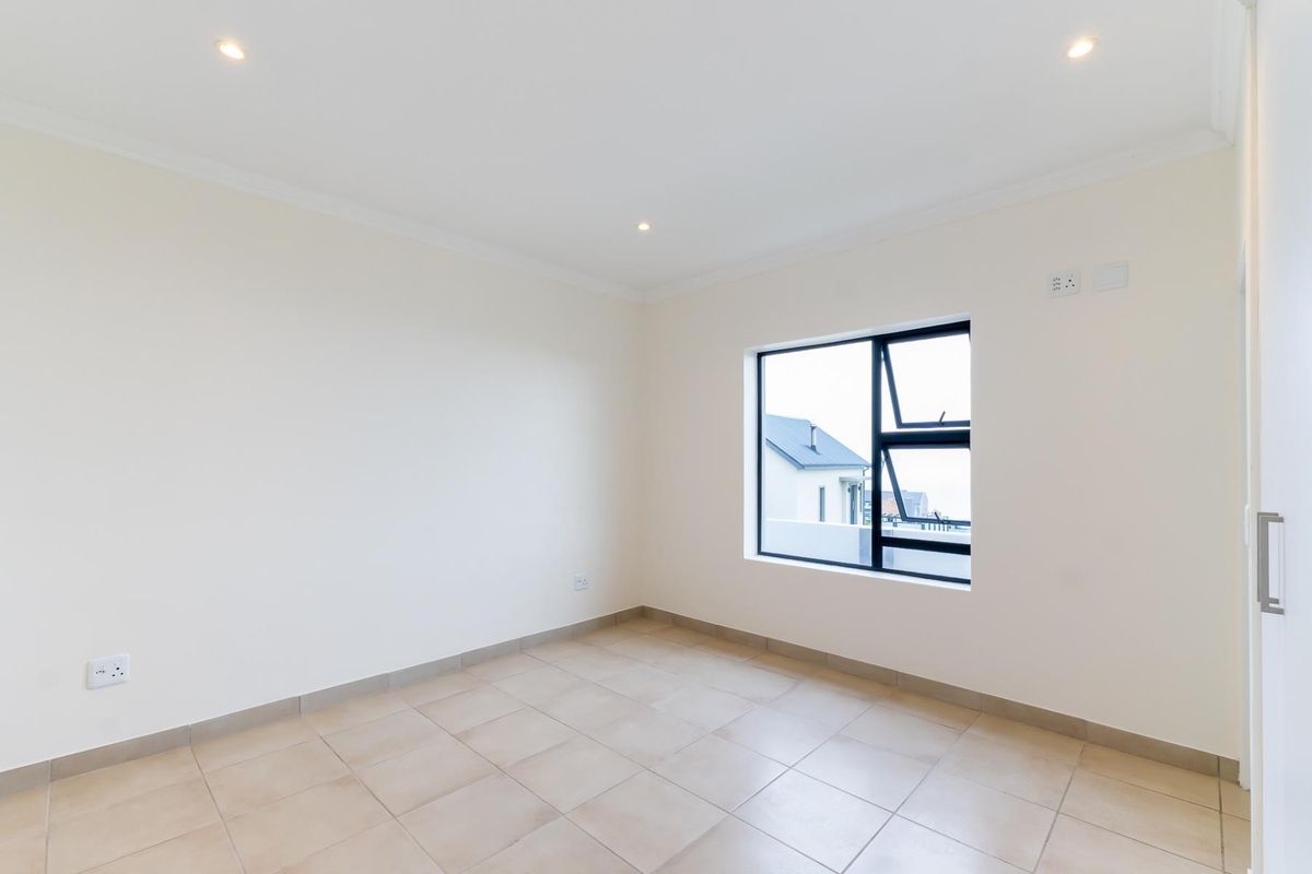 A bright, empty bedroom featuring neutral tiled flooring, recessed downlighting, and a modern aluminium-framed window.