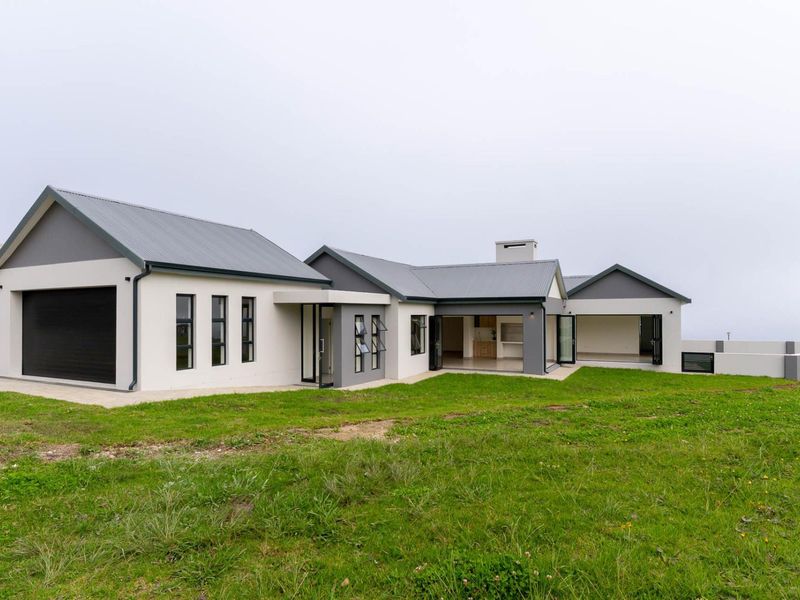 Rear view of a modern single-story house featuring a corrugated metal roof, integrated garage, and a covered patio area with bi-fold doors.