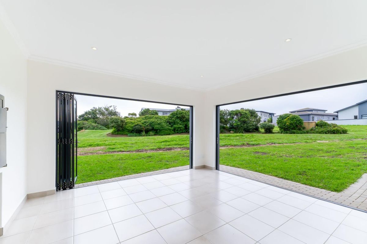 Bright, empty living area featuring large bi-fold doors that open onto a spacious garden, providing seamless indoor-outdoor flow and abundant natural light.