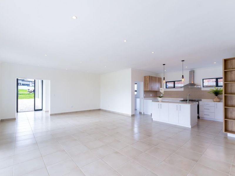 Spacious open-plan living and kitchen area featuring modern white cabinetry, a central island, tiled flooring, and recessed lighting throughout.