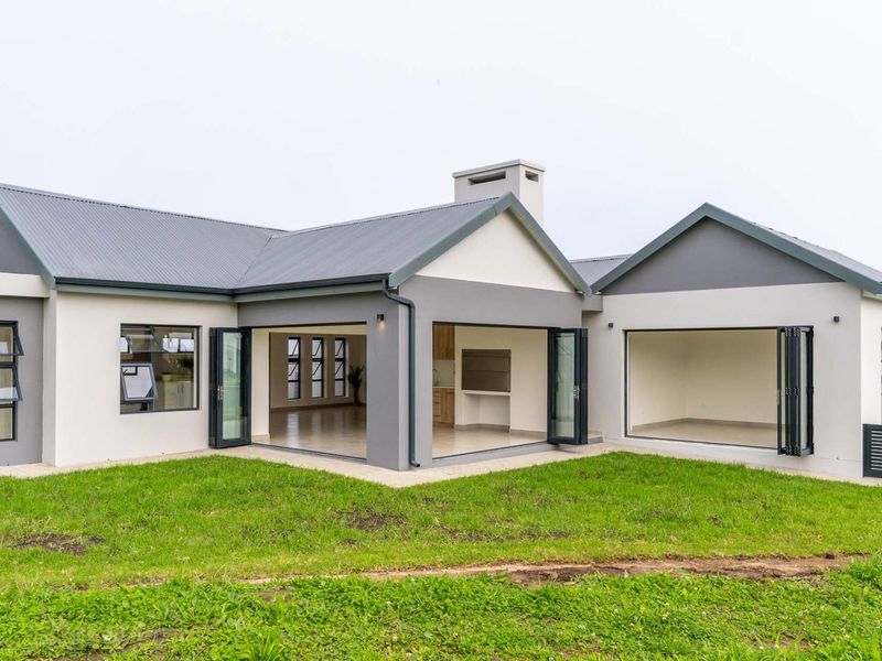 Rear view of a modern house featuring a metal roof, bi-fold doors opening to a patio, and a built-in outdoor braai area.