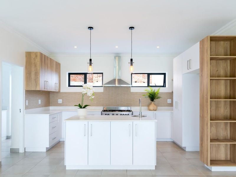 Modern kitchen featuring a central island, sleek white cabinetry with wood-tone accents, stainless steel appliances, and a tiled backsplash.