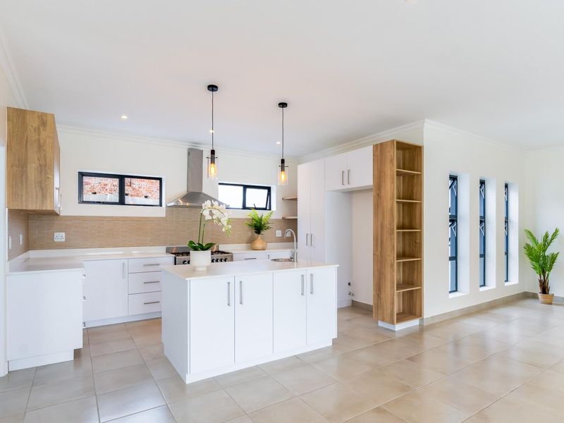 Modern kitchen featuring white cabinetry, a central island, stainless steel stove, extractor fan, tiled backsplash, and neutral floor tiles in an open-plan layout.