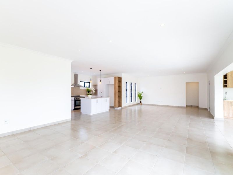 Spacious open-plan living area featuring neutral tiled flooring, recessed lighting, and a modern kitchen with built-in cabinetry and a central island.