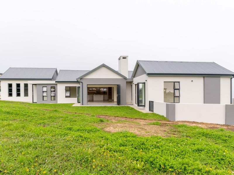 Rear view of a modern single-story house featuring a metal roof, chimney, and large bi-fold doors opening to an expansive, unfinished garden area.