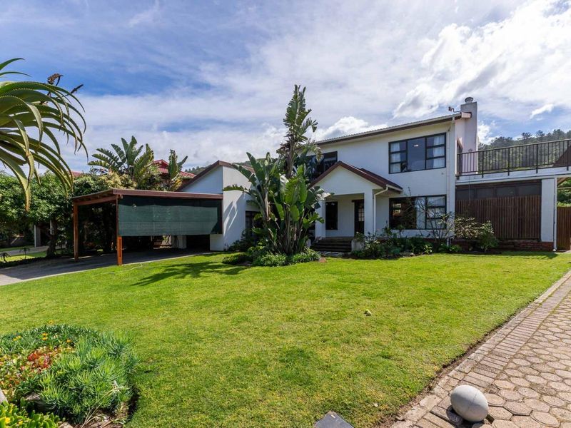 A well-maintained double-story residential property featuring a spacious front lawn, paved driveway, attached carport, and an upper-level balcony.