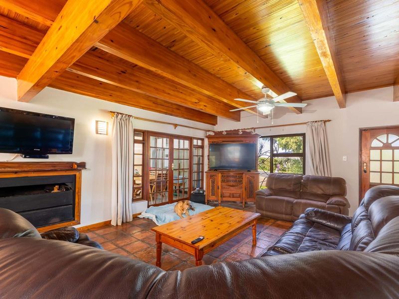 Spacious living room featuring exposed timber ceiling beams, terracotta floor tiles, and a built-in fireplace with direct access to the patio.