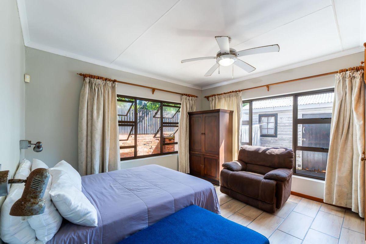 A well-lit bedroom featuring tiled flooring, a ceiling fan, and large windows that provide natural light and views of the exterior.
