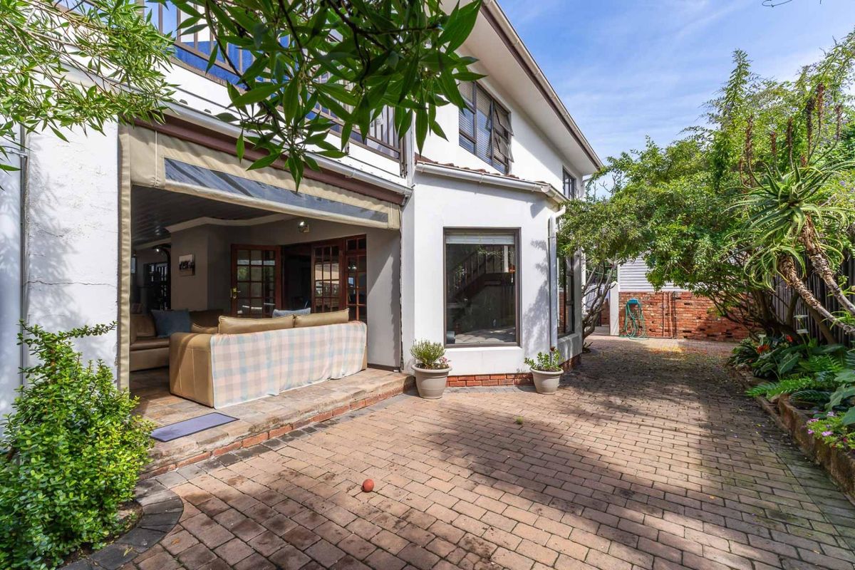 Rear exterior view featuring a brick-paved patio area, retractable awning, and established garden borders adjacent to the main living space.