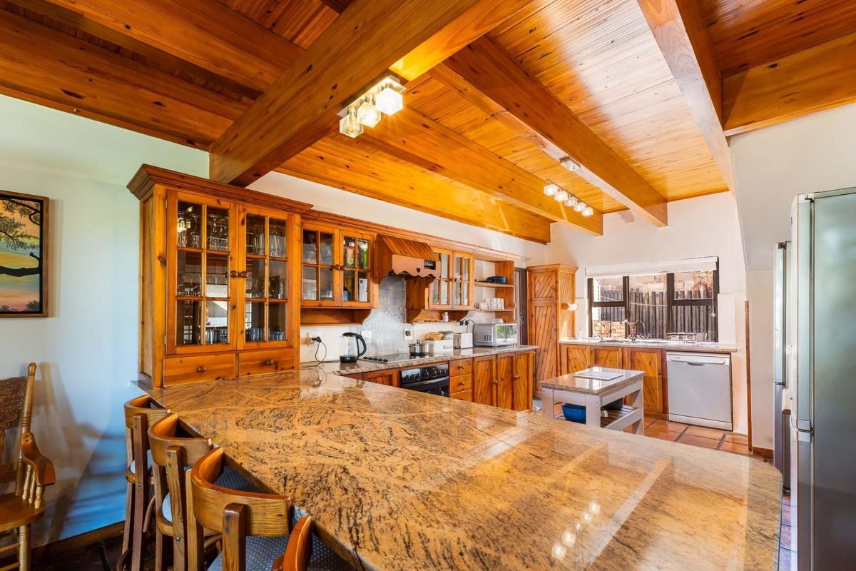 Spacious kitchen featuring extensive granite countertops, warm timber cabinetry, and exposed wooden ceiling beams, offering a rustic and functional cooking environment.