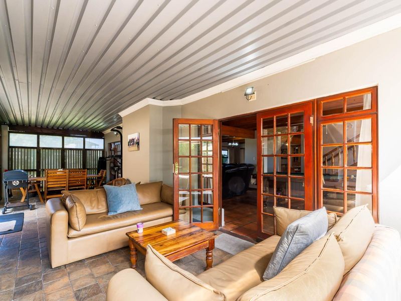 A spacious covered patio featuring tiled flooring, a corrugated metal ceiling, and classic timber-framed french doors providing access to the interior living area.