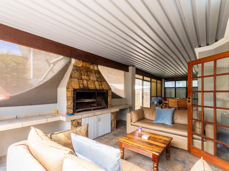 Covered patio area featuring a built-in stone-clad braai, tiled flooring, and a corrugated metal ceiling, providing a functional outdoor entertainment space.