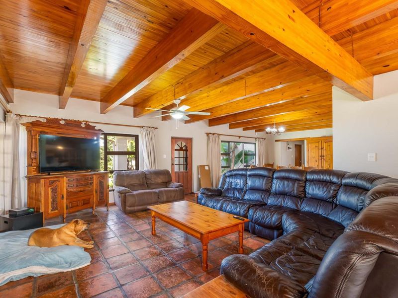 Spacious living room featuring a high exposed timber beam ceiling, terracotta tile flooring, and a ceiling fan, offering a warm and rustic atmosphere.