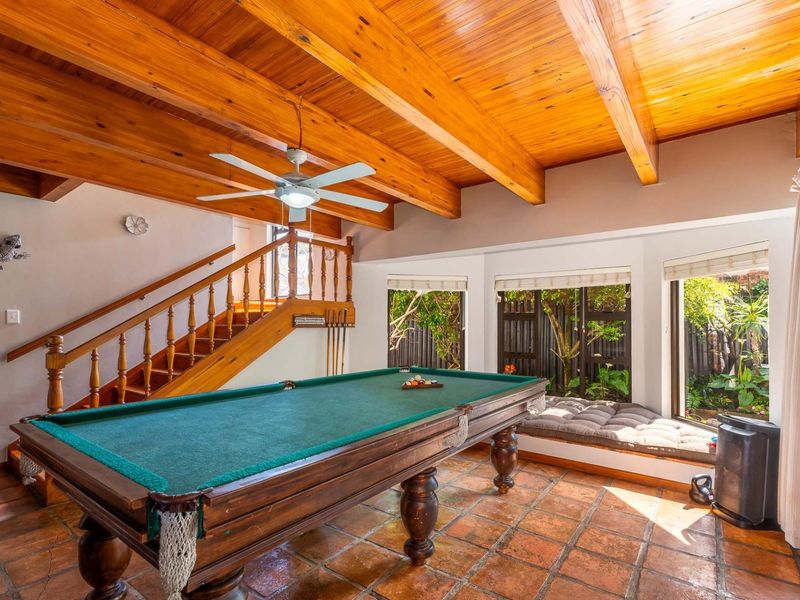 Spacious living area featuring exposed timber beam ceilings, terracotta tile flooring, a timber staircase, and a built-in window seat overlooking the garden.