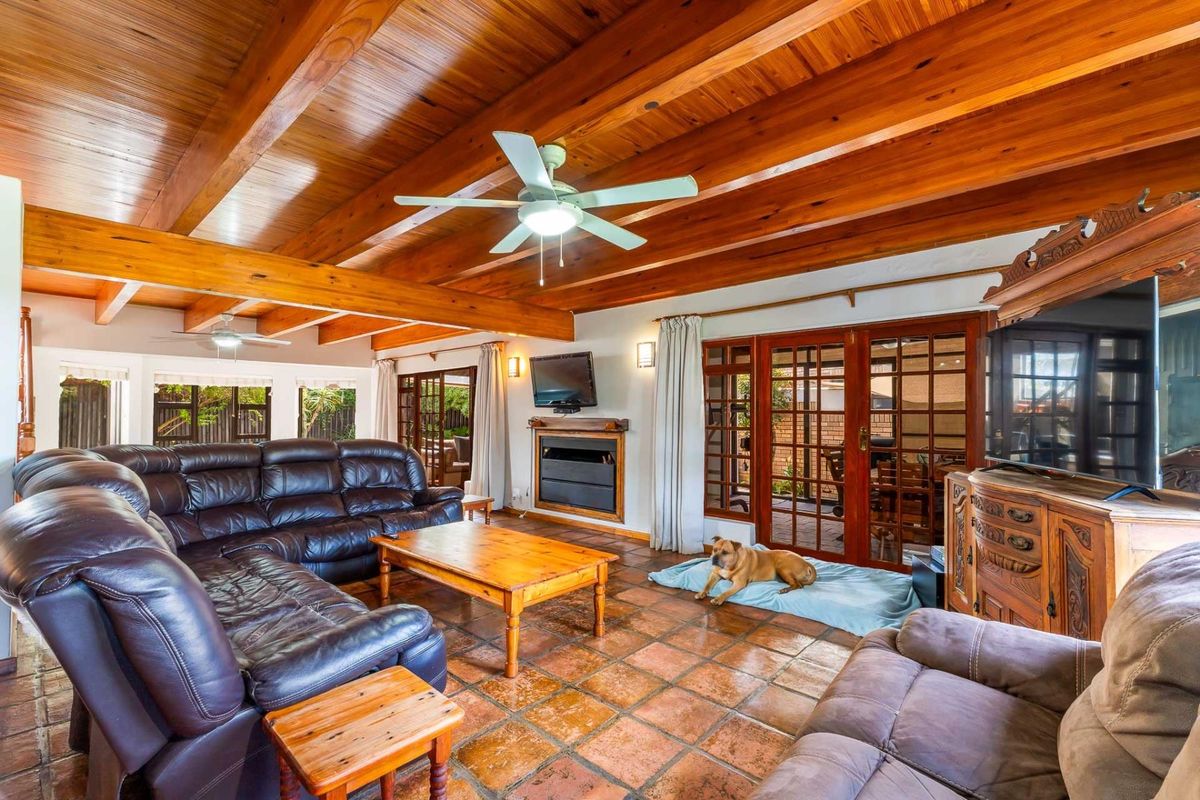 Spacious living room featuring exposed timber ceiling beams, terracotta floor tiles, a built-in fireplace, and direct access to the patio through french doors.
