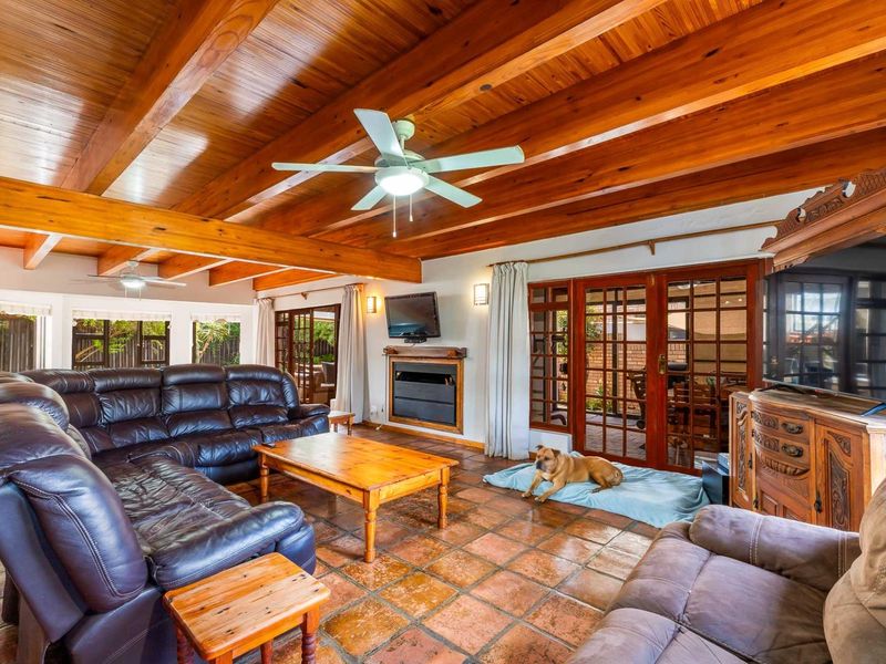 Spacious living room featuring exposed timber ceiling beams, terracotta floor tiles, a built-in fireplace, and direct access to the patio through french doors.
