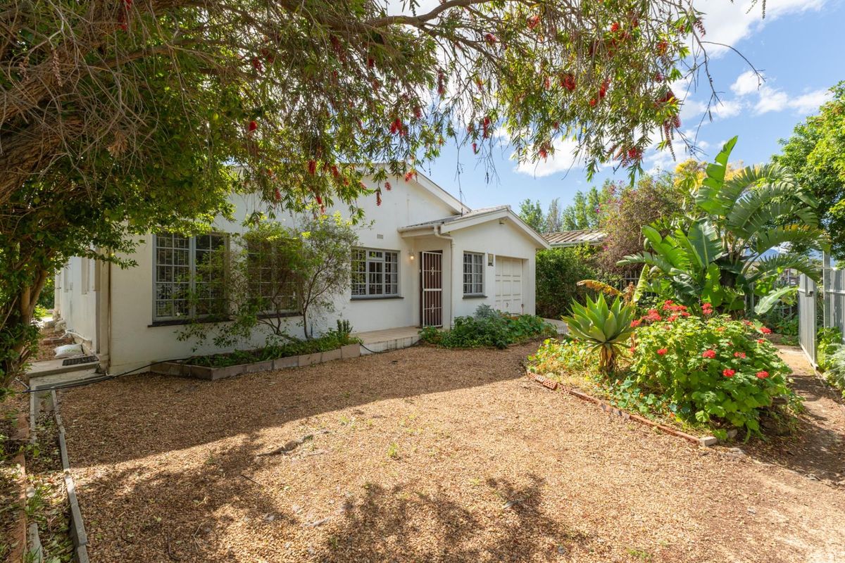 A rear view of the house featuring a gravel yard, established garden, and a single garage with a security gate entrance.