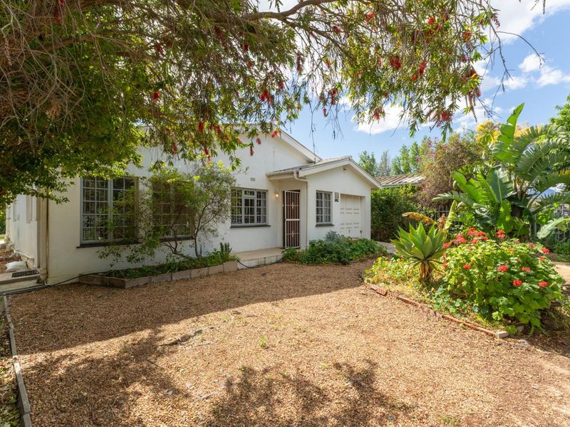 A rear view of the house featuring a gravel yard, established garden, and a single garage with a security gate entrance.