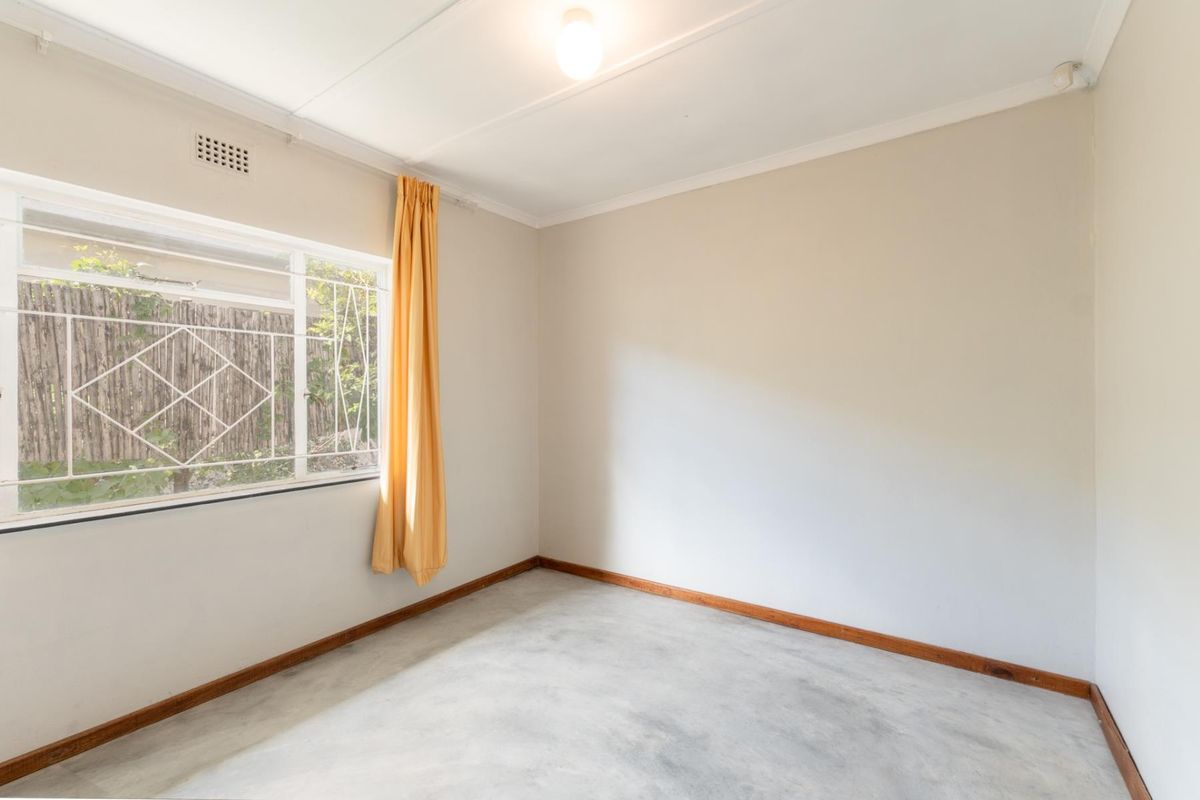 A clean, empty bedroom featuring neutral walls, a large window with security bars, and simple flooring, ready for personalization.