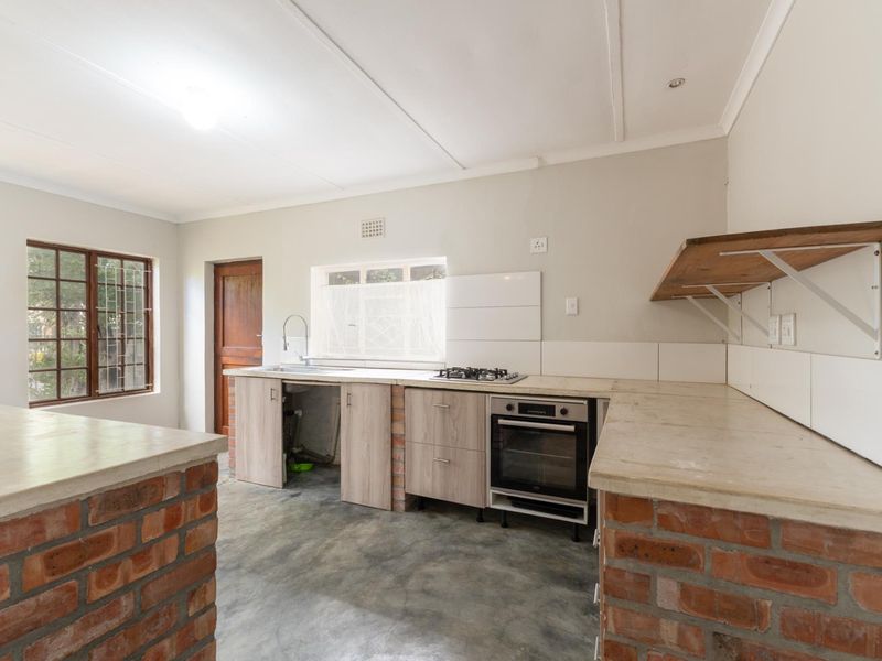 A functional kitchen featuring exposed brick cabinetry, concrete flooring, a built-in oven, gas hob, and a stainless steel sink with open storage space.