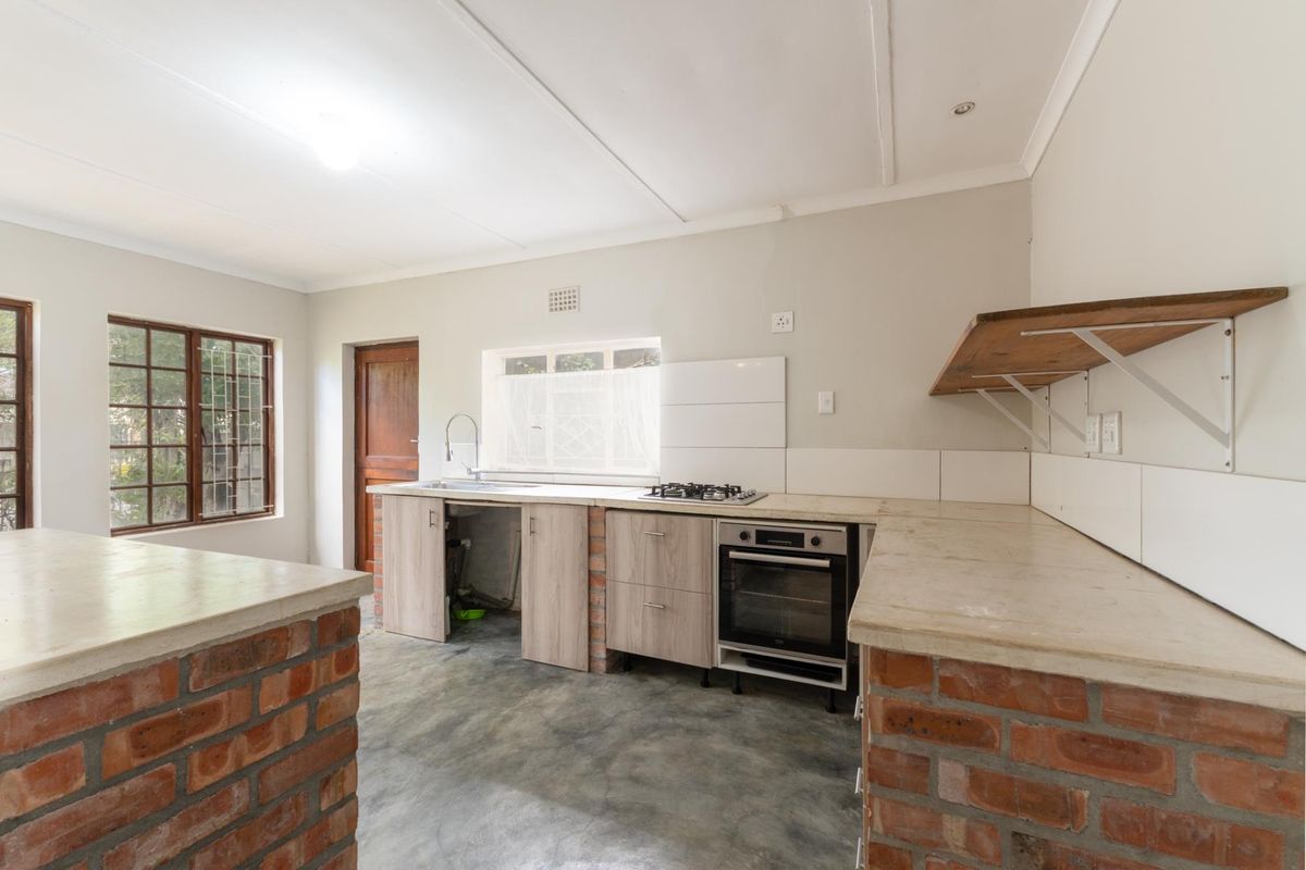 A functional kitchen featuring exposed brick cabinetry, concrete flooring, a built-in oven, gas hob, and a stainless steel sink with open storage space.