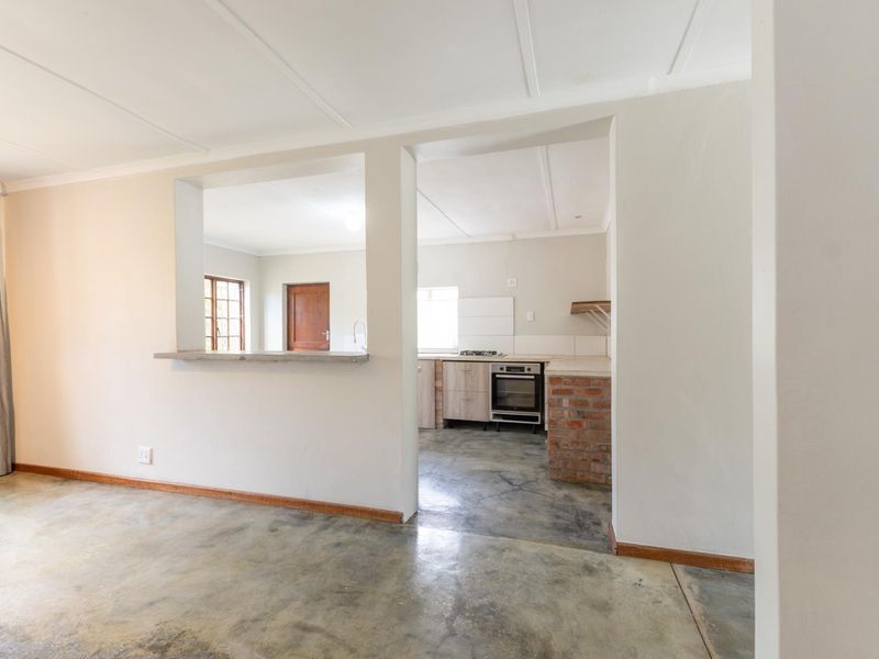 Open plan living area featuring concrete flooring, a serving hatch, and a kitchen with built-in oven, hob, and exposed brick detailing.