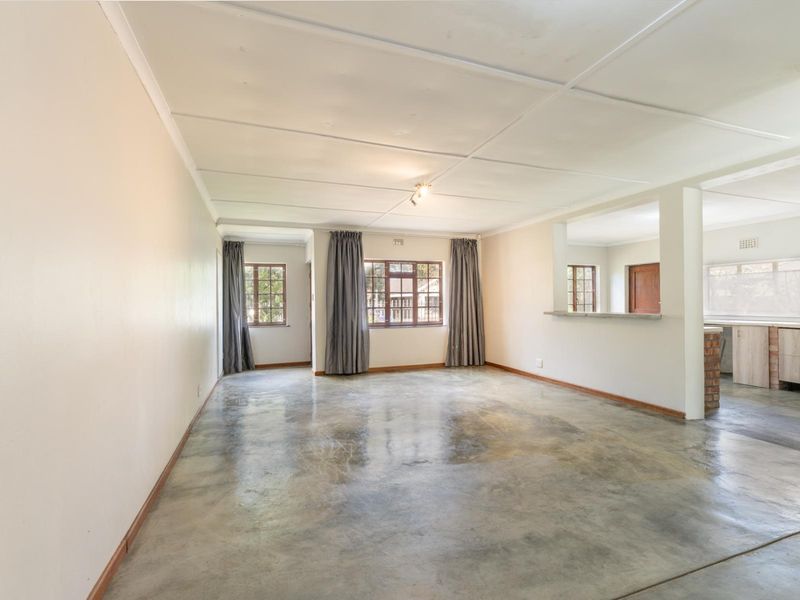 Spacious open-plan living area featuring polished concrete floors, large windows, and a convenient serving hatch connecting to the kitchen space.