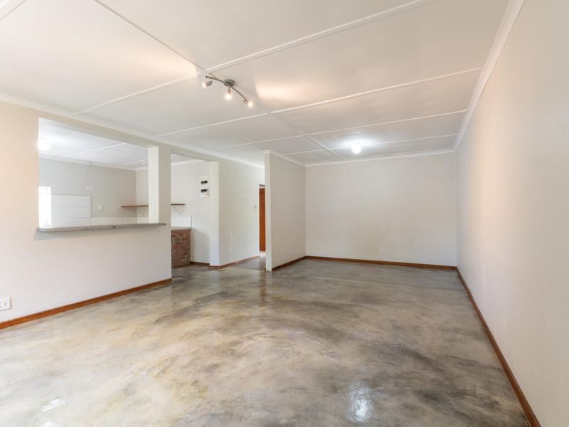 An empty open-plan living area featuring polished concrete floors, a pass-through kitchen window, and neutral walls, offering a blank canvas for renovation.