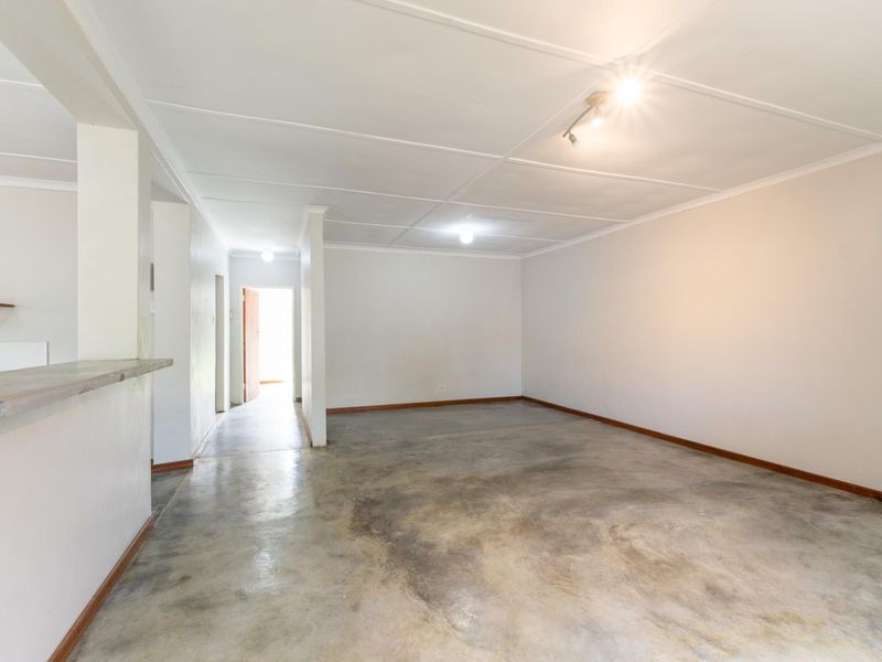 An empty, open-plan living area featuring concrete flooring, a breakfast bar, and a neutral color palette, offering a blank canvas for renovation.