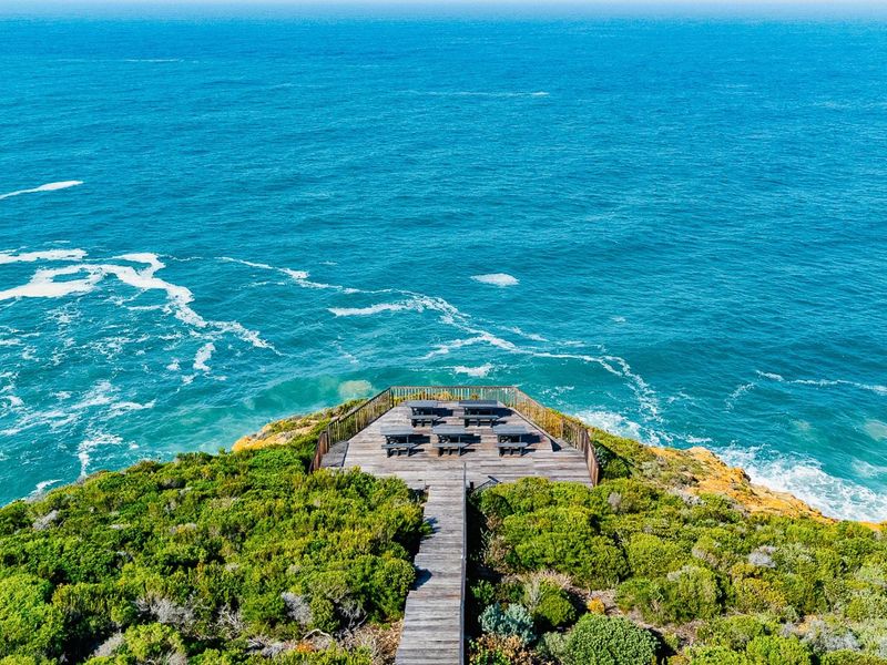 An elevated aerial view of a wooden observation deck and walkway situated on a coastal cliff overlooking the ocean.
