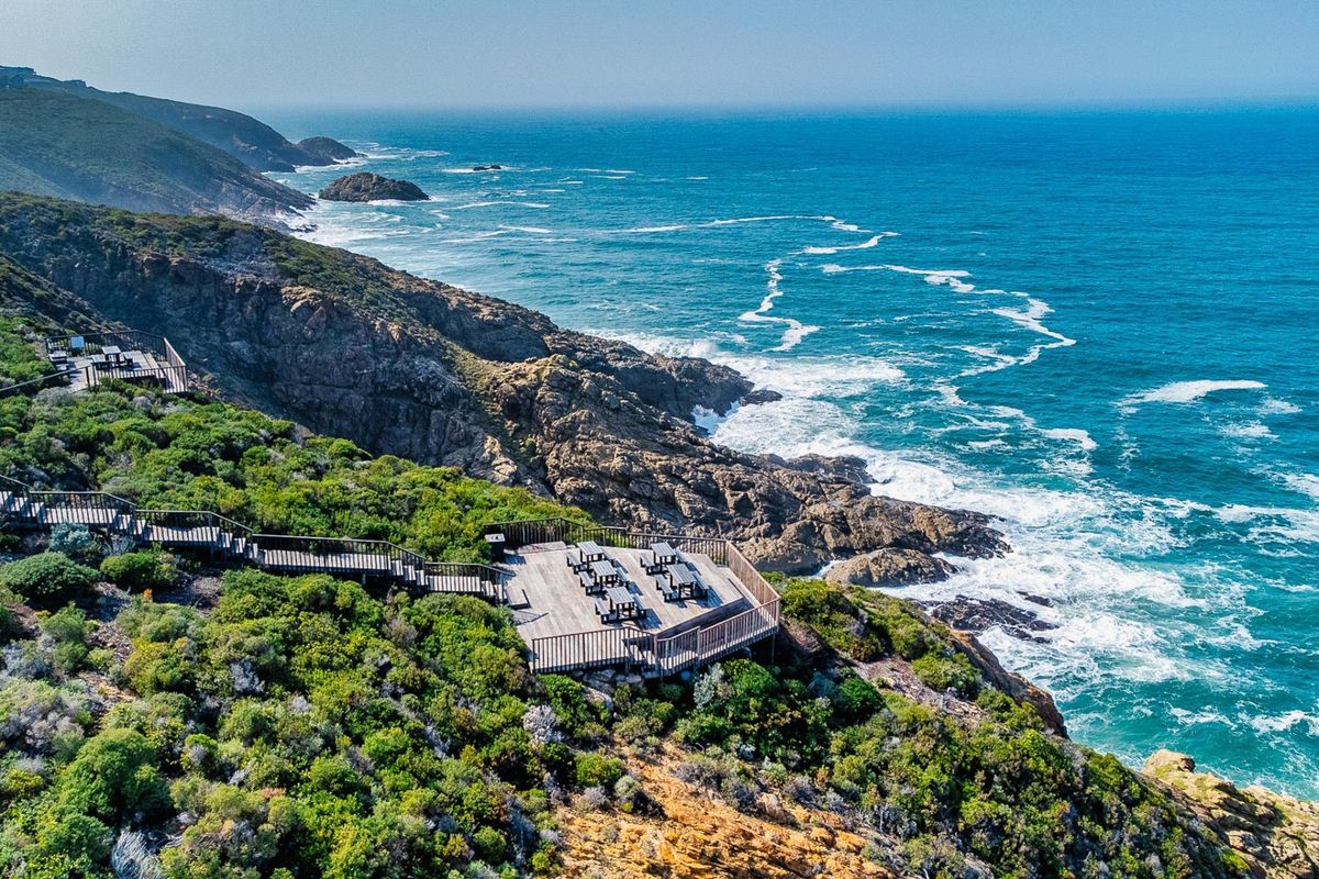 An elevated aerial view of a timber viewing deck perched on a rugged coastal cliff overlooking the ocean.
