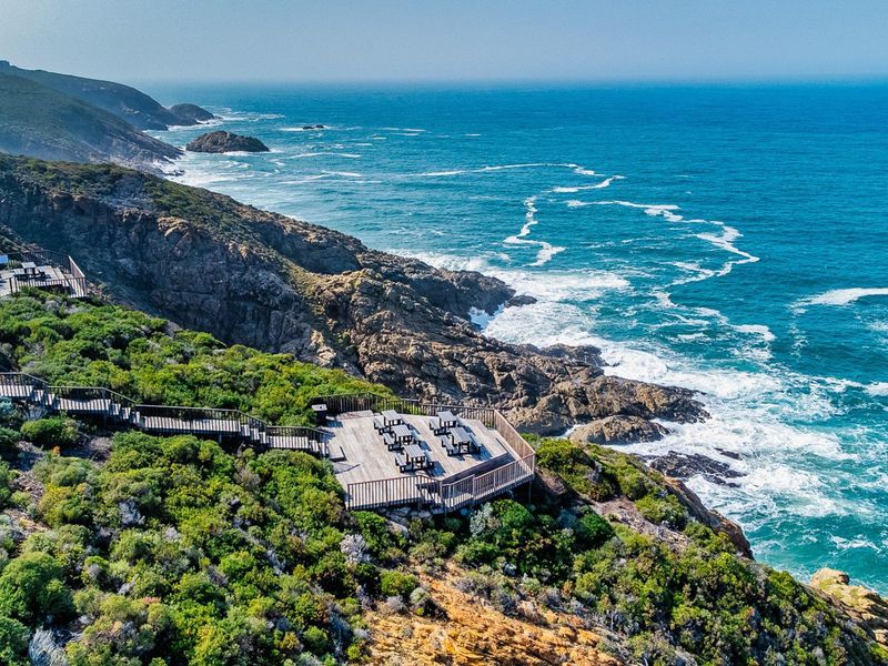 An elevated aerial view of a timber viewing deck perched on a rugged coastal cliff overlooking the ocean.