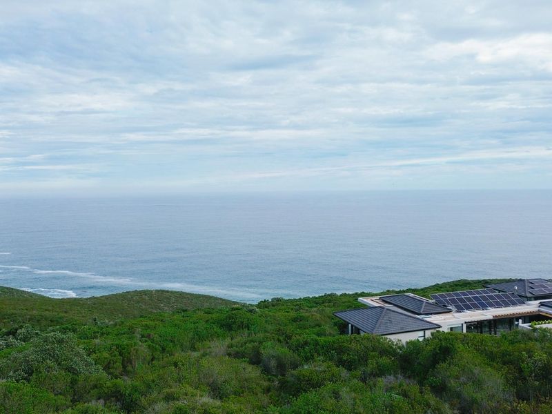 Elevated coastal view overlooking the ocean and surrounding natural landscape, featuring a modern residence with integrated solar panels.
