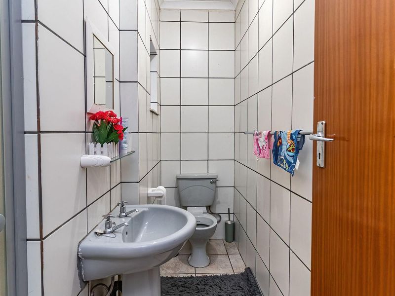 A compact bathroom featuring a pedestal basin, toilet, and shower enclosure with full-height wall tiling.