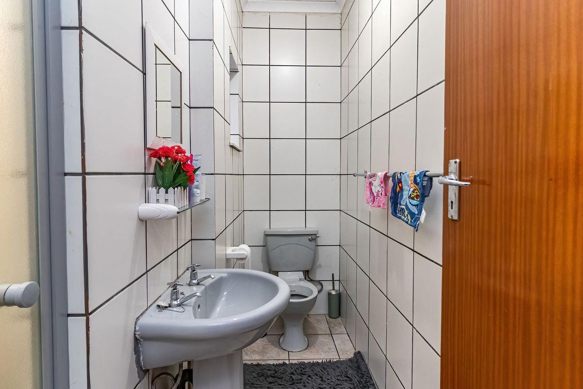 A compact bathroom featuring a pedestal basin, toilet, and shower enclosure with full-height wall tiling.