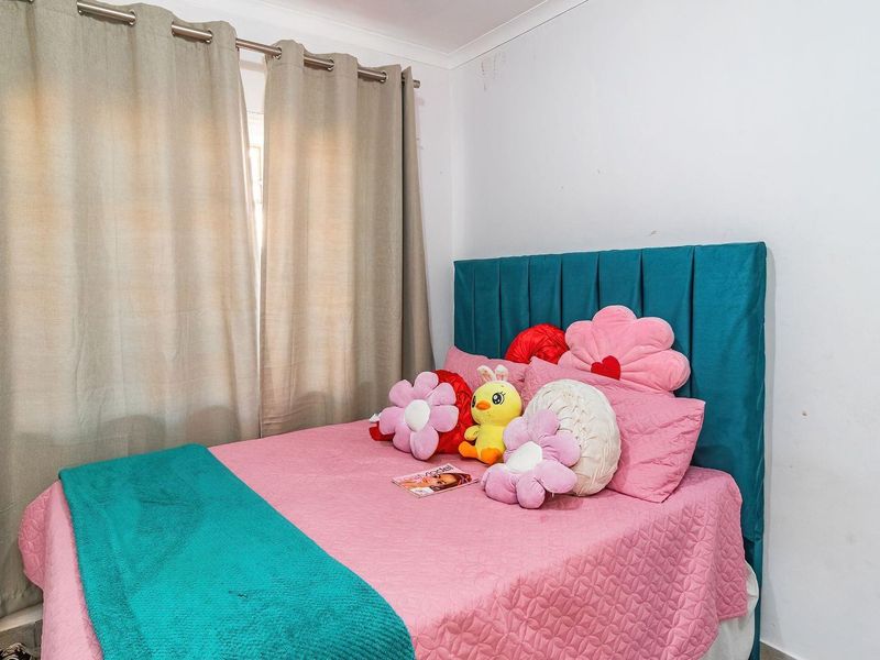 A bedroom featuring neutral curtains and a teal upholstered headboard, with visible scuffing on the walls requiring minor cosmetic attention.