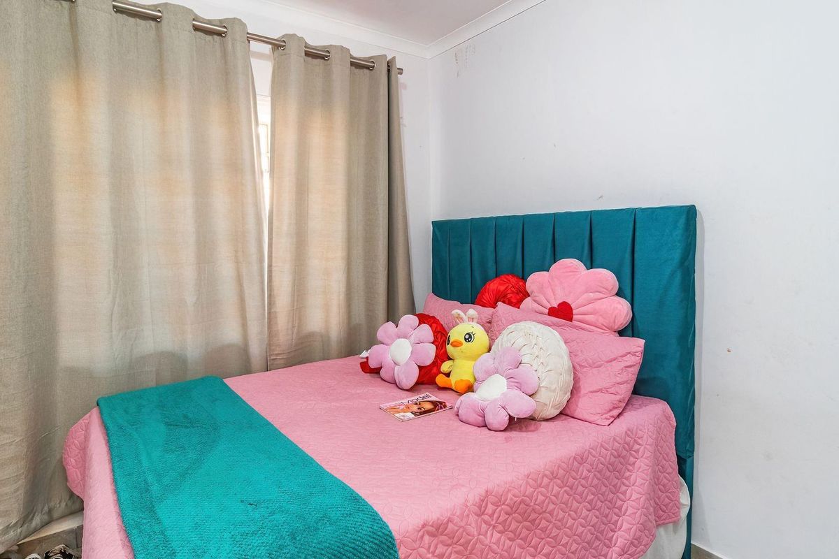A bedroom featuring neutral curtains and a teal upholstered headboard, with visible scuffing on the walls requiring minor cosmetic attention.