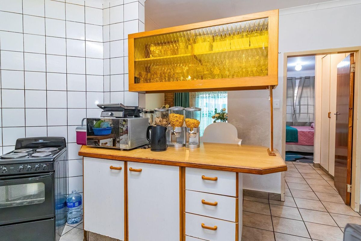 A dated kitchen featuring tiled splashbacks, wooden cabinetry, a breakfast counter, and a freestanding stove, with direct access to the hallway.