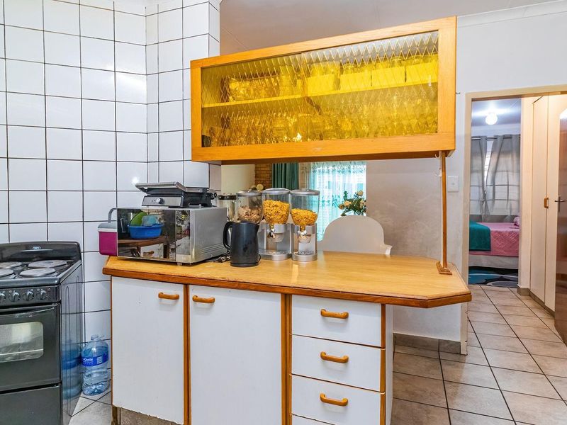 A dated kitchen featuring tiled splashbacks, wooden cabinetry, a breakfast counter, and a freestanding stove, with direct access to the hallway.
