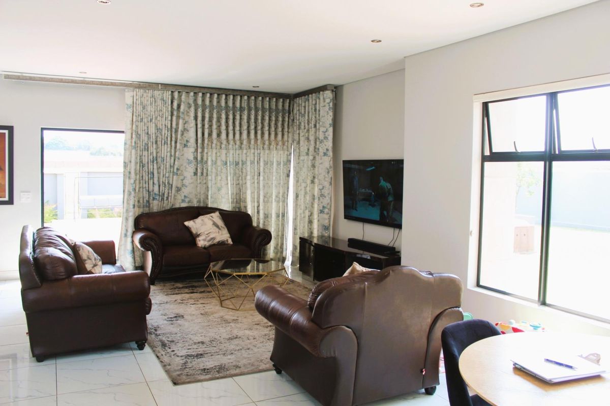 A bright and spacious living room featuring large windows, tiled flooring, and recessed downlighting, creating a comfortable and well-lit living environment.